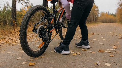 One caucasian children walk with bike in autumn park. Little girl walking black orange cycle in forest. Kid goes do bicycle sports. Biker motion ride with backpack and helmet. Mountain bike hard tail.