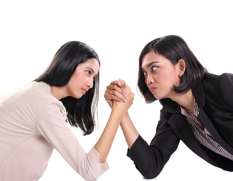Two female business workers face each other in arm wrestling battle, white background