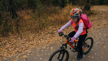 One caucasian children rides bike road in autumn park. Little girl riding black orange cycle in...
