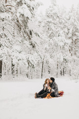 young couple on a date in the winter forest is heated by the fire and drink cocoa