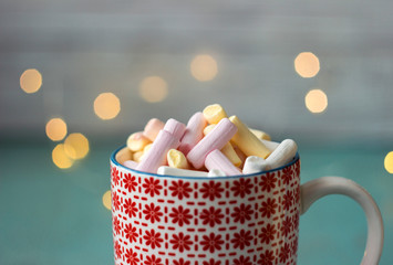 Pink, yellow and white marshmallow in the Cup, top view, Christmas lights, wooden background