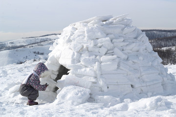 The child holds a snowball squatting at the entrance to the home of Eskimos - igloo