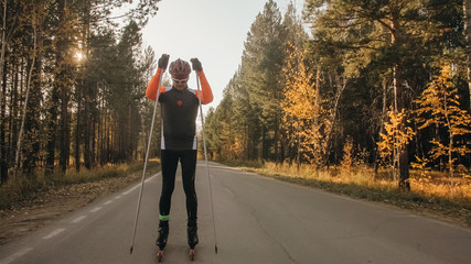 Training an athlete on the roller skaters. Biathlon ride on the roller skis with ski poles, in the helmet. Autumn workout. Roller sport. Adult man riding on skates.