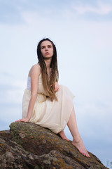 Fototapeta na wymiar Beautiful girl sitting on a rock in a light dress.
