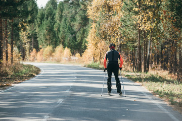 Obraz premium Training an athlete on the roller skaters. Biathlon ride on the roller skis with ski poles, in the helmet. Autumn workout. Roller sport. Adult man riding on skates.