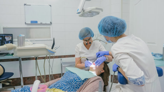 Woman at dentist clinic gets dental treatment to fill a cavity in a tooth. Dental restoration and composite material polymerization with UV light and laser. The doctor works with an assistant.