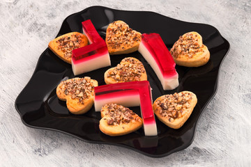 Homemade heart-shaped cookies. Congratulations on the day of lovers. Glass black plate with reflection. Red and white jelly. Light background.