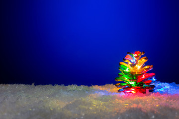 Frozen fir cone with colourful garland lights on blue snowy background with copy space. Christmas background