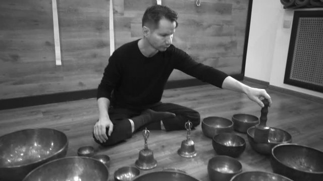 Man sits on floor in lotus position and plays Tibetan bowls