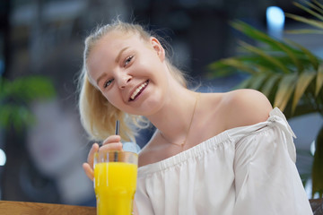 Portrait of happy young girl drinking orange juice in cafe. Leisure and people concept