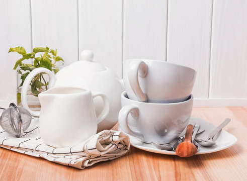 Different tableware, plates, cups standing near the white wooden wall