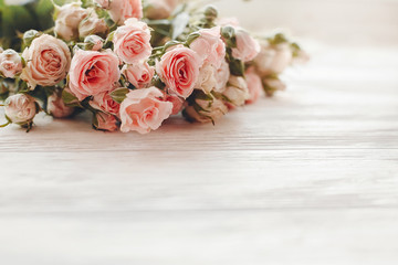 Pink small roses on wooden background in light, space for text. Floral greeting card mockup....
