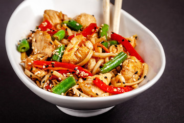 Concept of Asian cuisine. Wheat noodles from durum flour with vegetables and chicken. Carrots, bell peppers, green beans, white and black sesame. Japanese or Chinese dish.