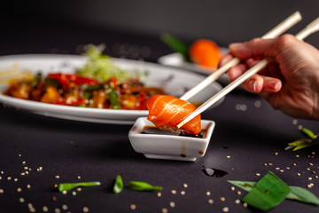 Concept of Asian cuisine. The girl is in a Chinese or Japanese restaurant sushi, holds wooden sticks in his hands. Dunk sushi in soy sauce. Different Asian dishes are on the table