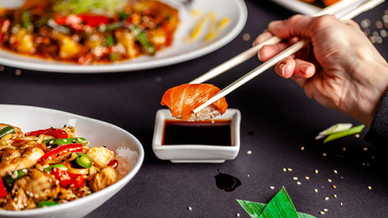 Concept of Asian cuisine. The girl is in a Chinese or Japanese restaurant sushi, holds wooden sticks in his hands. Dunk sushi in soy sauce. Different Asian dishes are on the table