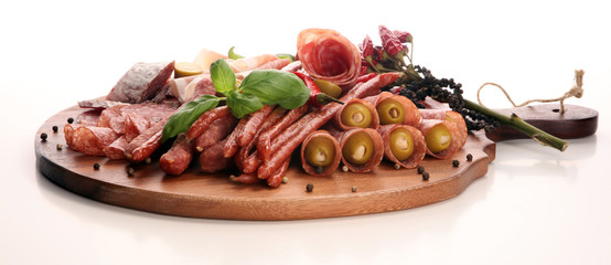 Food tray with delicious salami, pieces of sliced prosciutto crudo, sausage and basil. Meat platter with selection