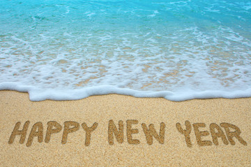 Happy new year written on sandy beach.