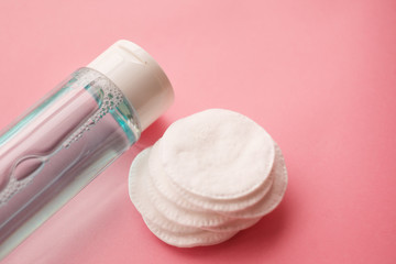 bottle with tonic or micellar cleansing water with fresh herbs and flowers and cotton pads on pink...