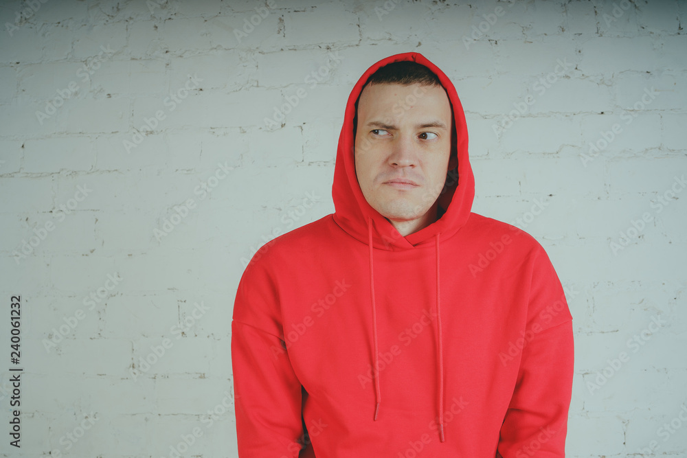 Wall mural Handsome guy posing by a brick wall. Crazy man in a red hoodie