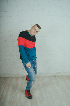 Emotional portrait of a guy in full height, crazy guy posing for the camera. Short hair, clean skin. Street style clothing sweatshirt and jeans. The concept of good mood. Model grimaces