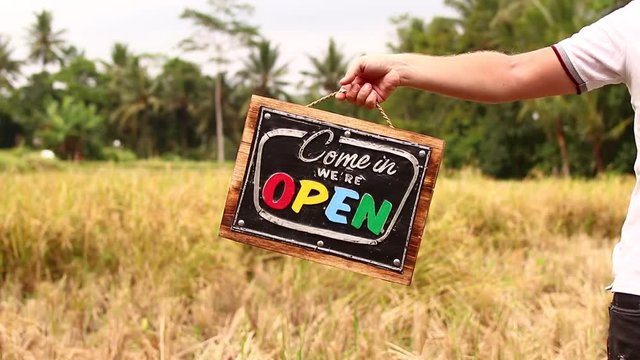 Open sign board in a man hands on a tropical nature background. Shooted on Bali island, full HD.