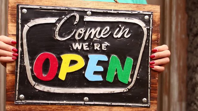 Open sign board in a woman hands on a tropical nature background. Shooted on Bali island, full HD.