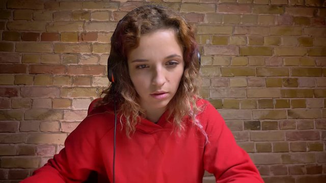 Close-up portrait of young blogger in headphones in front of camera reading and talking on bricken wall background.