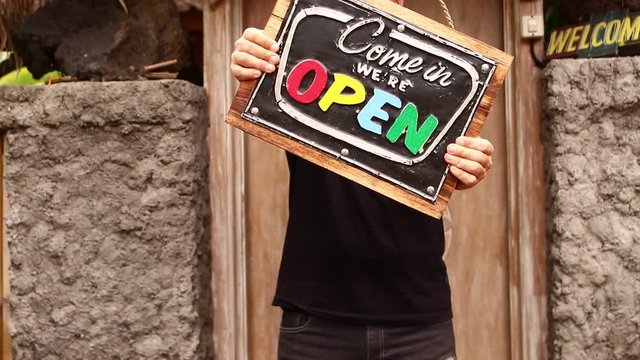 Open sign board in a man hands on a tropical nature background. Shooted on Bali island, full HD.