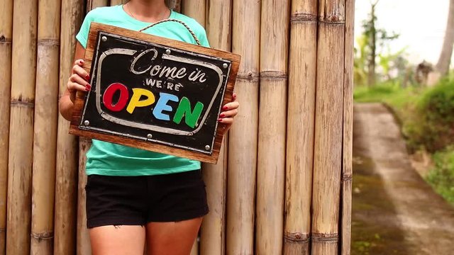 Open sign board in a woman hands on a tropical nature background. Shooted on Bali island, full HD.