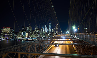 Fototapeta na wymiar Long exposure picture of cars passing over the illuminated Brooklyn Bridge at night. Manhattan skyline in the background, New York city, USA.