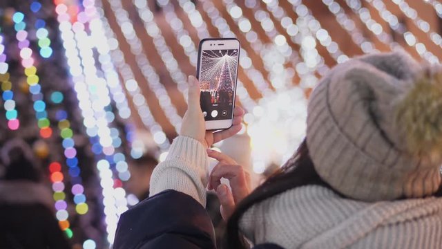 A woman photographs a city Christmas tree on her smartphone