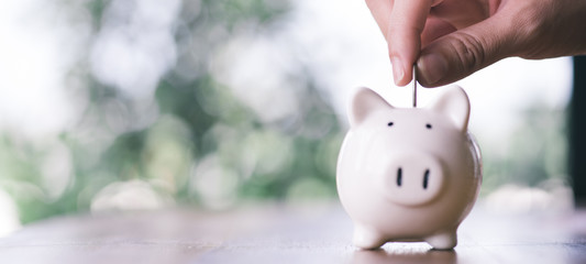 Hand putting coin on piggy bank.