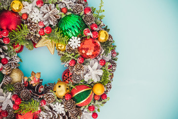 Top view Beautiful traditional bright Christmas wreath decorated with pine cones, spruce branches,berries, balls, stars, decorative beers on blue background isolated. Close up, flat lay. Copy space.