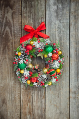 Top view Beautiful hand made bright Christmas wreath decorated with pine cones, spruce branches,berries, balls, stars and decorative beers on rustic wooden background, flat lay. Vertical. Copy space.