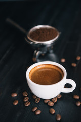 Fresh tasty espresso cup of hot coffee with coffee beans and Coffee maker on dark background