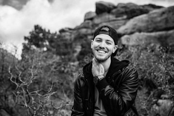 Portrait of Young Good Looking Casual Traveling Handsome Man Smiling Near Ancient Desert Red Rocks in Jacket Outside