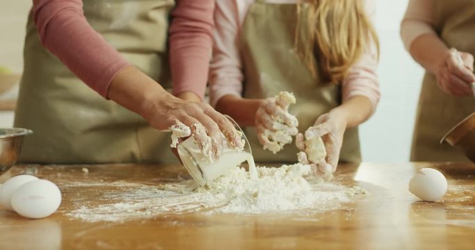 Close up of the Caucasian female and kid's hands making and kneading a dough on the table. Mother teaching her daughter.
