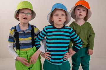 Three children in colored clothes and colorful hats posing in front of photographer in the studio during the summer holidays. Brothers amicably cope with work