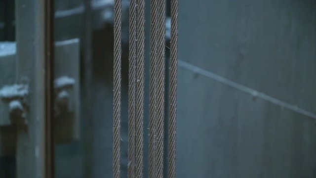 Closeup: Strong suspended cables inside elevator shaft move, carrying the car