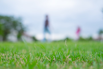 Blurred image of people having leisure activity on green field.  Picture with selective focus on grass in foreground.