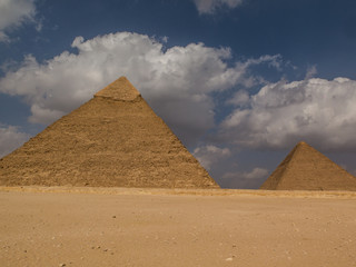 Two ancient pyramids under a blue sky with clouds
