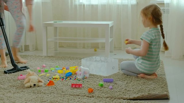 mom and daughter, a young woman cleans up with a vacuum cleaner, a little girl with blond hair collects toys, the designer in a container, helps mom