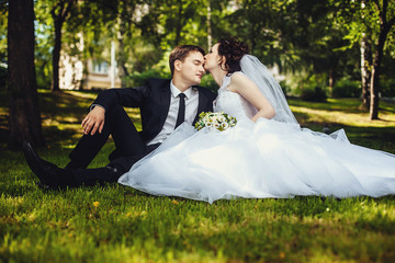 Happy bride and groom sit summer on the grass in the Park and enjoy each other