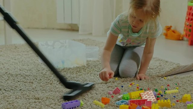 mom and daughter, a young woman cleans up with a vacuum cleaner, a little girl with blond hair collects toys, the designer in a container, helps mom