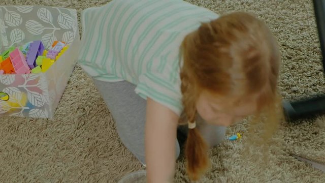 mom and daughter, a young woman cleans up with a vacuum cleaner, a little girl with blond hair collects toys, the designer in a container, helps mom