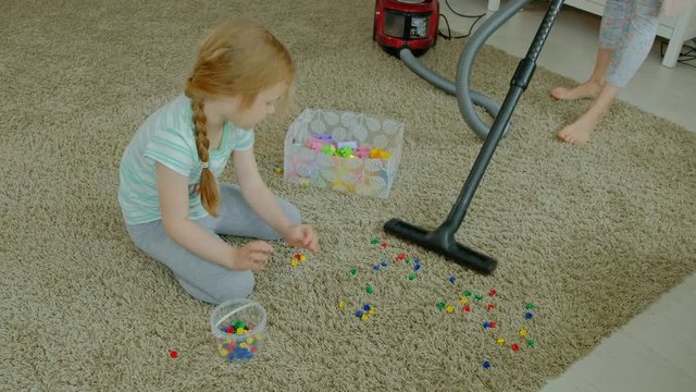 mom and daughter, a young woman cleans up with a vacuum cleaner, a little girl with blond hair collects toys, the designer in a container, helps mom