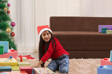  A little girl wearing Christmas hat playing with gift box 	