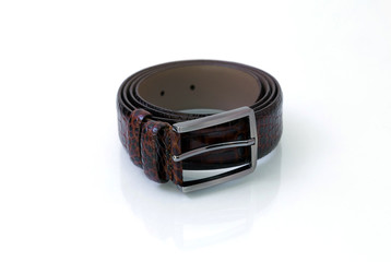 Rolled brown leather men's belt with reptile skin texture isolated on white glassy surface, closeup. Fashion concept
