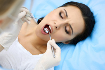 Young female patient visiting dentist office.Beautiful woman with healthy straight white teeth sitting at dental chair with open mouth during oral checkup while doctor working at teeth