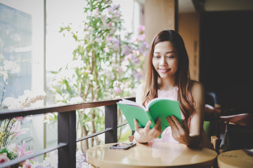 Young smile beautiful woman sits at a window in a cafe and read a book happily